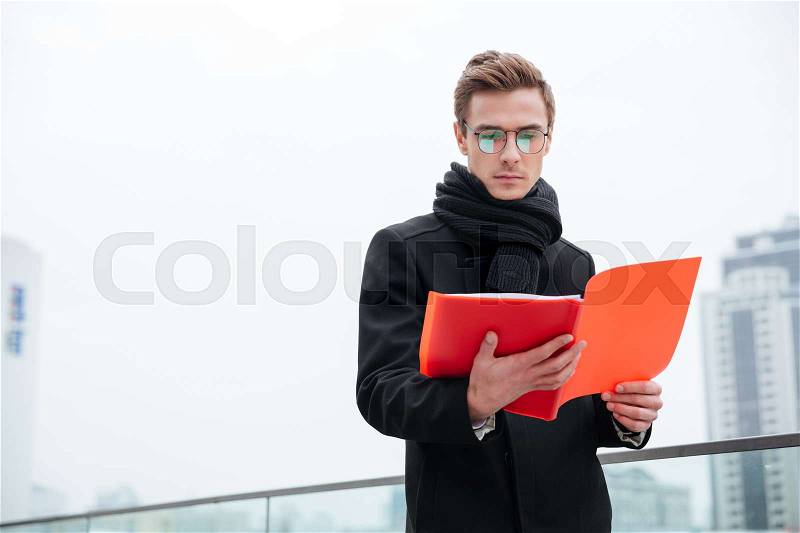 Serious Business man in glasses and warm clothes reading documents outdoors, stock photo