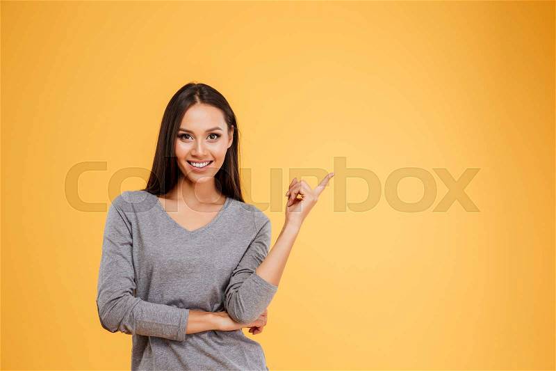 Young model pointing upwards in studio. isolated orange background, stock photo