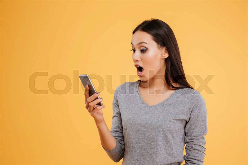 Surprised model with phone. looking at phone. isolated orange background, stock photo