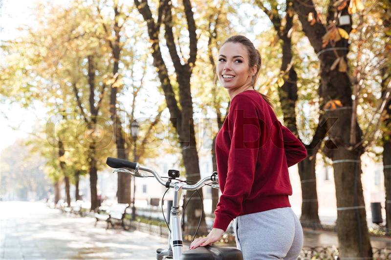 Photo of pretty lady dressed in sweater walking with her bicycle outdoors. Look aside, stock photo