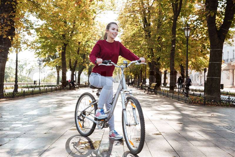 Happy lady dressed in sweater walking with her bicycle outdoors. Look aside, stock photo