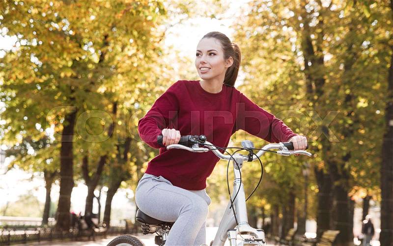 Beautiful woman dressed in sweater walking with her bicycle outdoors. Look aside, stock photo
