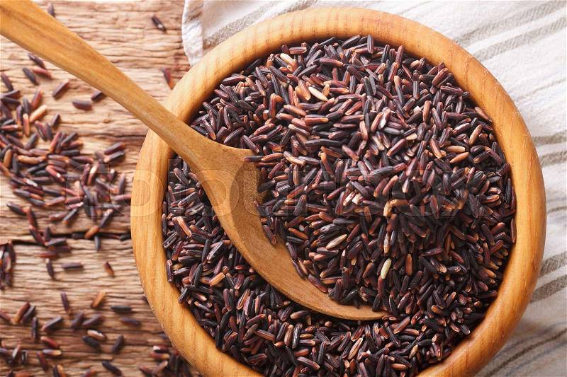 Healthy wild long black rice close up in a wooden bowl and spoon. horizontal view from above , stock photo