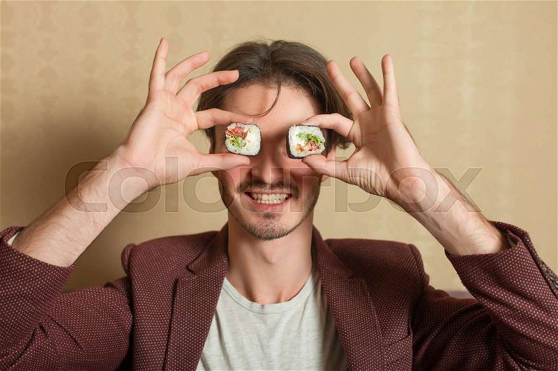 Smiling man hold sushi rolls instead of eyes. Traditional japanese seafood, stock photo