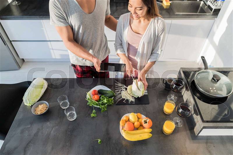 Young Couple In Kitchen, Asian Woman Cooking Food Breakfast, Hispanic Man Show Cell Smart Phone Modern Apartment Interior, stock photo