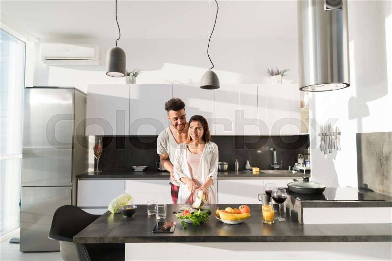 Young Couple Embrace In Kitchen, Hispanic Man And Asian Woman Hug Modern Apartment Interior, stock photo