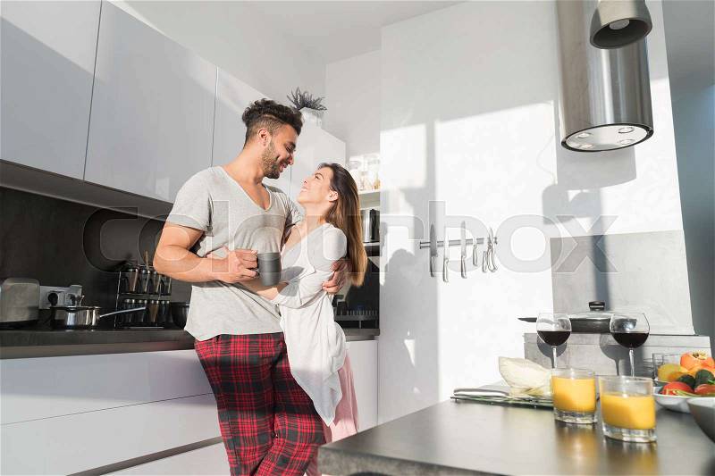 Young Couple Embrace In Kitchen, Hispanic Man And Asian Woman Hug Morning Breakfast Modern Apartment Interior, stock photo