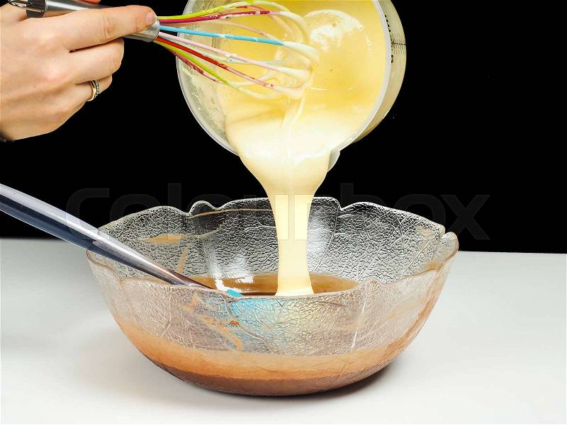 Female person pouring Gogl-Mogl, into a glass bowl with chocolate, with hand whisker from plastic bowl, isolated on black, stock photo