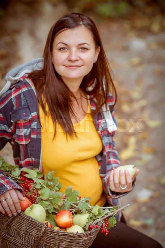 Pregnant woman with a basket of fruit in the autumn park, stock photo