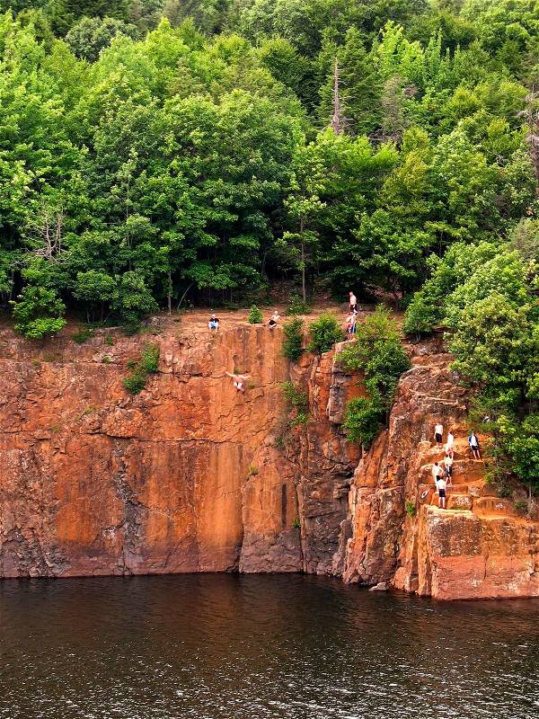 Some crazy kids cliff jumping off the side of a mountain from 60 feet up into the water below, stock photo
