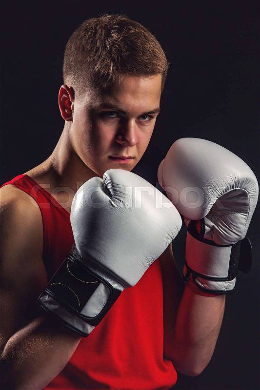 Young handsome boxer sportsman in red boxer suit and white gloves standing on black backgound. Copy space, stock photo