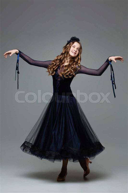Beautiful teenager ballroom dancer with long blond hair in long dark blue dress making curtsy. Studio shot on grey background. Copy space, stock photo