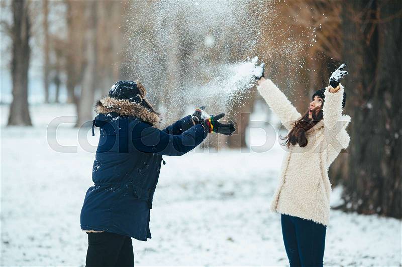 Boy and girl playing with snow in snow-covered park, stock photo