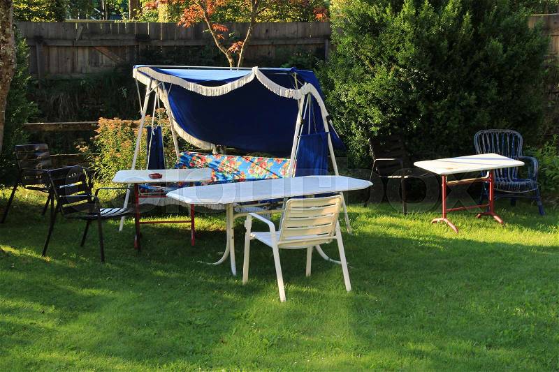 Garden furniture, a striking rocking chair with floral motif for more than one person, plastic chairs and tables in the back yard in the residential area in the village in the beautiful summer, stock photo