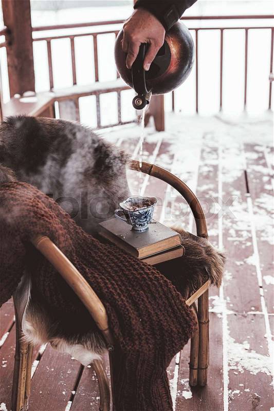 Chair with fur cover on a porch deck of a log cabin with snow. Making hot tea. Cold winter relax weekend, stock photo