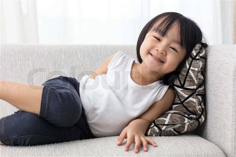 Happy Asian Chinese little girl lying down on the sofa in the living room at home, stock photo