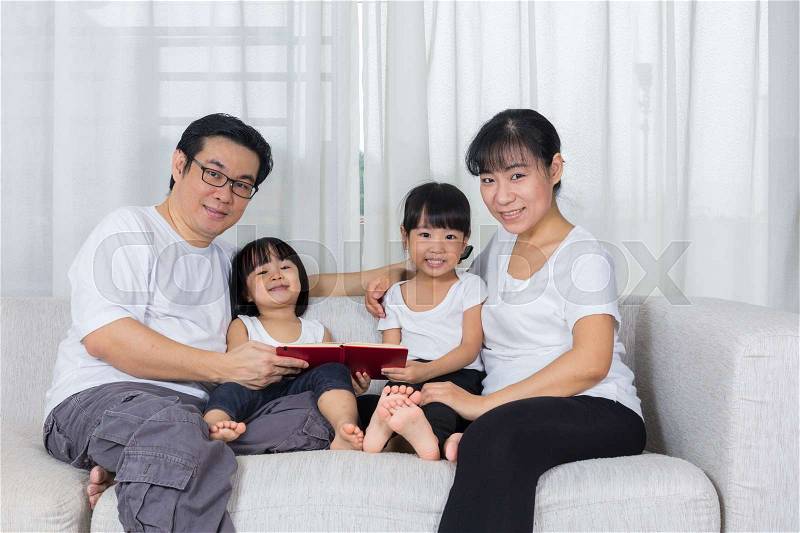 Happy Asian Chinese family reading book on the couch in the living room at home, stock photo