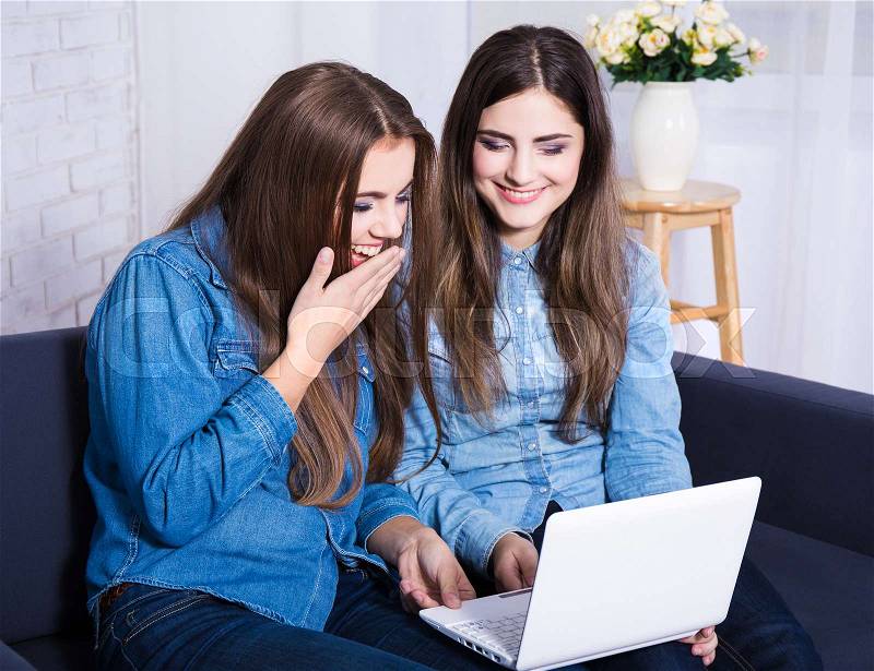 Online shopping concept - cheerful girls searching something on laptop at home, stock photo