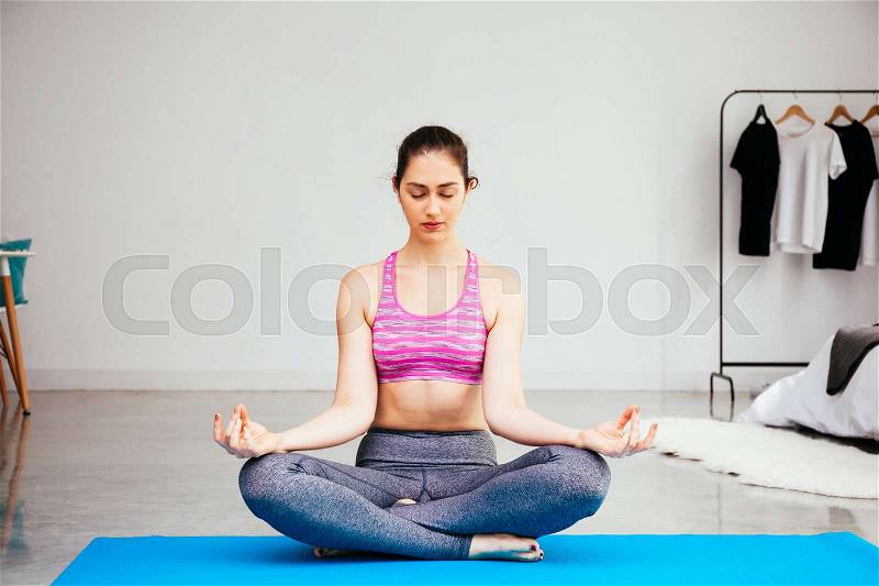 Young Caucasian woman doing yoga meditation in lotus pose position at home, stock photo