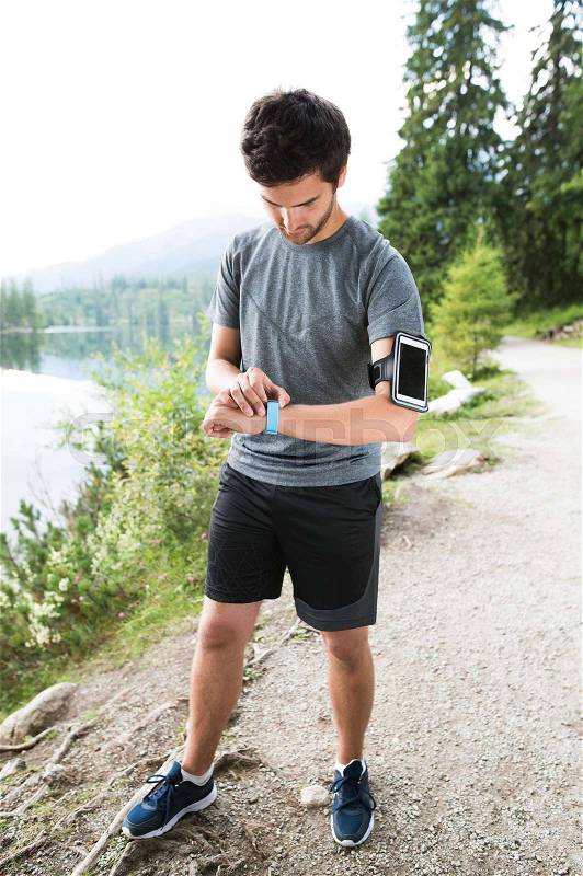 Young runner at the lake in green nature with smart phone and smartwatch. Using a fitness app for tracking weight loss progress, running goal or summary of his run, stock photo