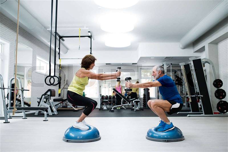 Beautiful fit senior couple in gym working out with weights and squatting at the same time, stock photo