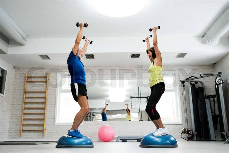 Beautiful fit senior couple in gym working out with weights, stock photo