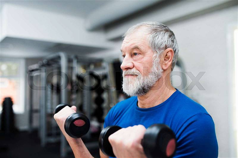 Senior man in sports clothing in gym working out with weights, stock photo