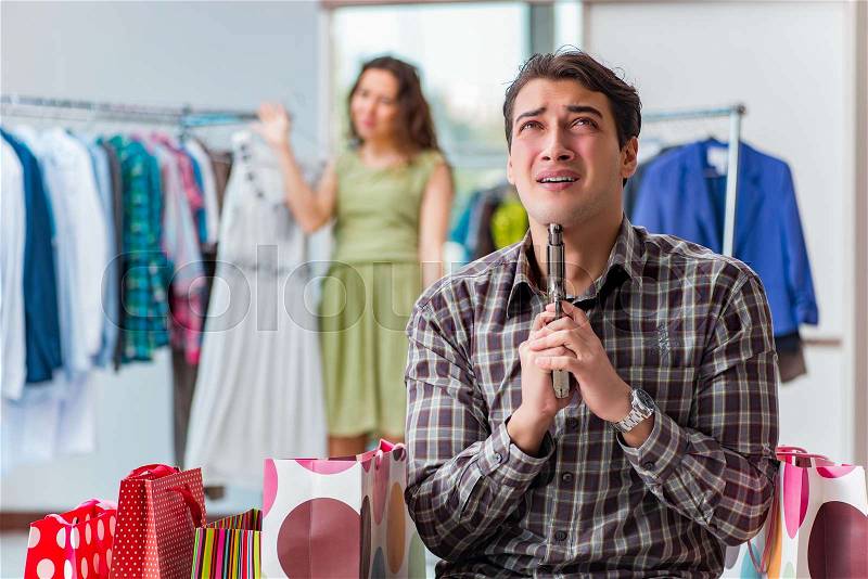 Man fed up with wife shopping in shop, stock photo