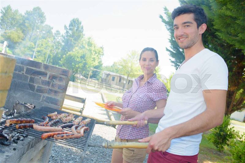 Couple cooking sausages on a barbeque, stock photo