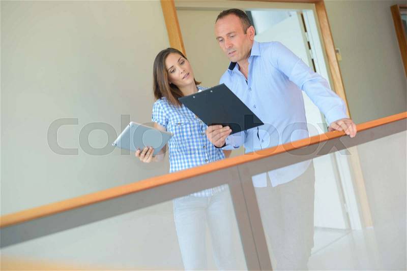 Man and woman in corridor looking at clipboard, stock photo