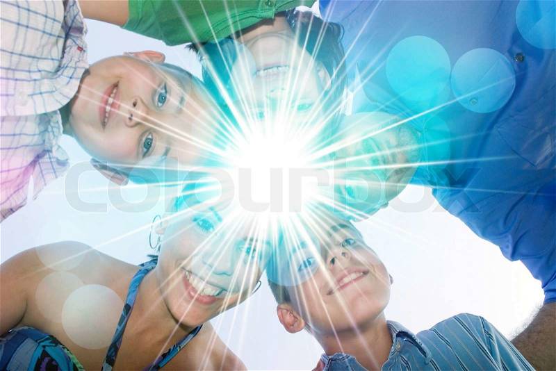 A happy family in a circular huddle formation with a bright lens flare in the center with copy space for your text or image, stock photo