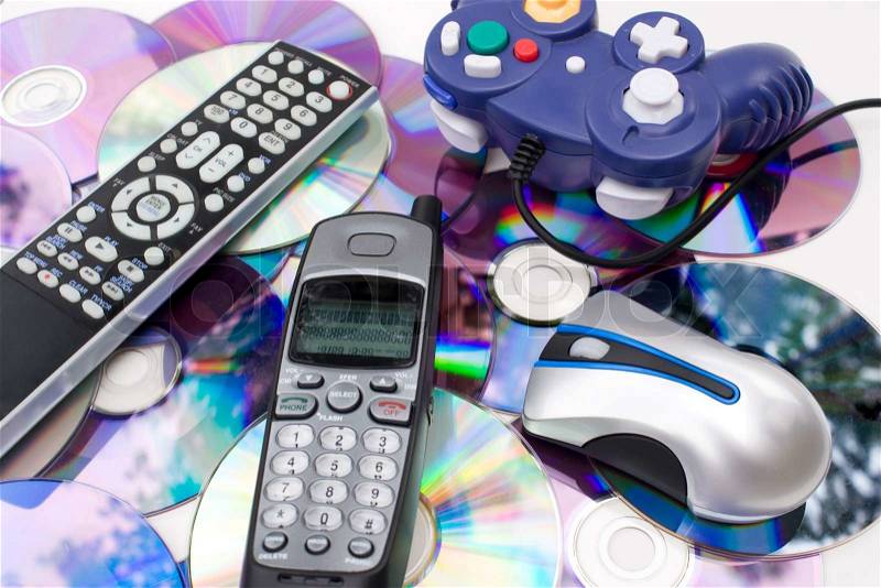 Remote control wireless computer mouse cordless telephone and video game controller over a bed of dvd disks isolated over white, stock photo