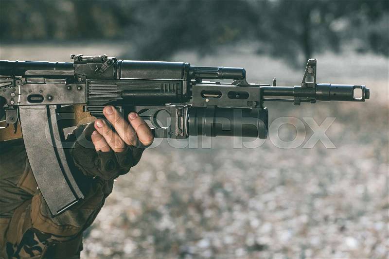 The soldier in the performance of tasks in camouflage and protective gloves holding a gun. War Zone, stock photo