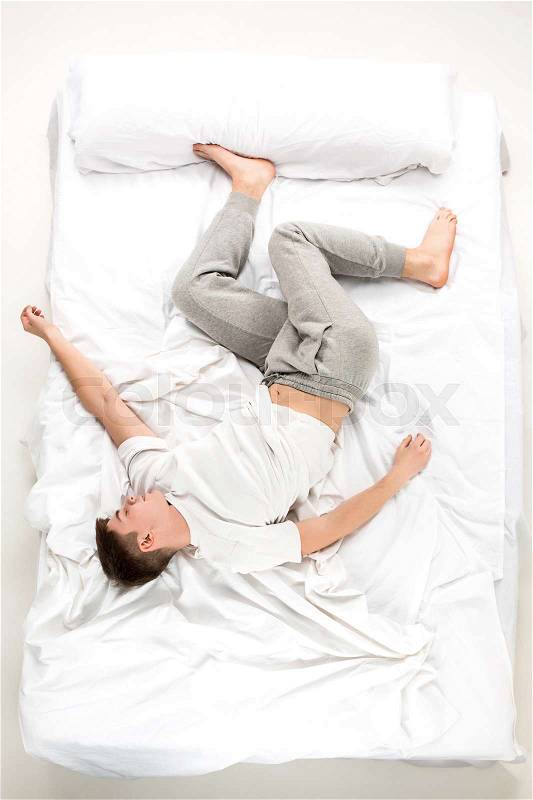 The young man lying in a white bed, top view, stock photo