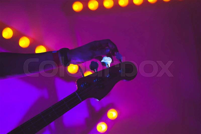 Live music background, guitarist tunes electric bass guitar, closeup photo with soft selective focus and colorful illumination, stock photo