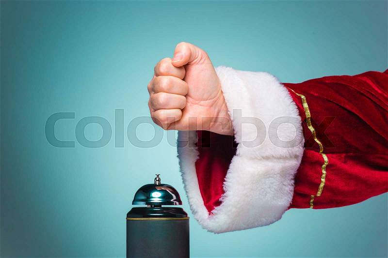 The hand of santa claus pressing on the bell on blue background, stock photo