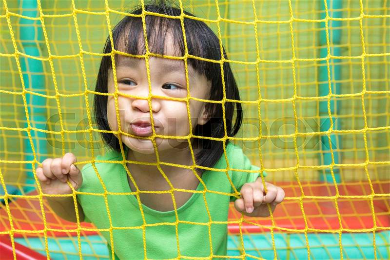 Happy Asian Chinese little girl playing behind the net at indoor playground, stock photo
