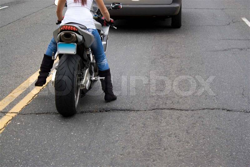 A young woman sitting on a motorcycle stopped in traffic at a red light, stock photo