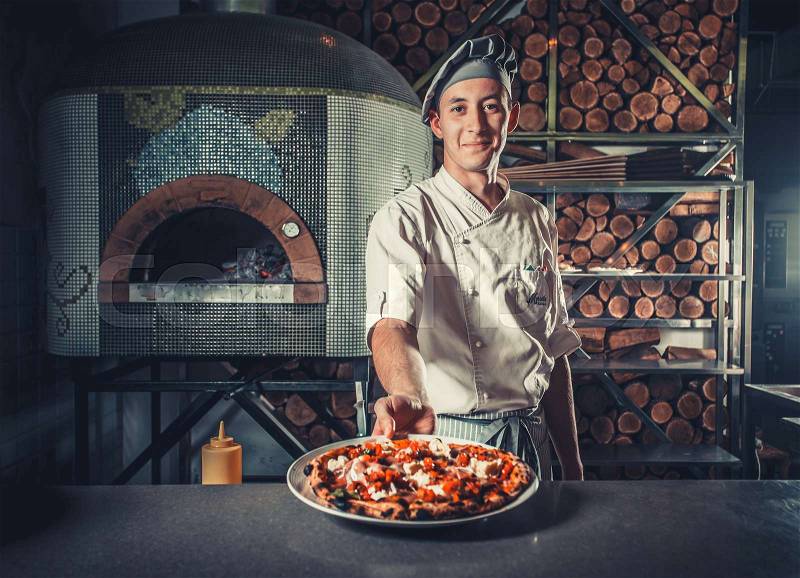 Young male cook holding fresh cooked pizza on white plate, stock photo