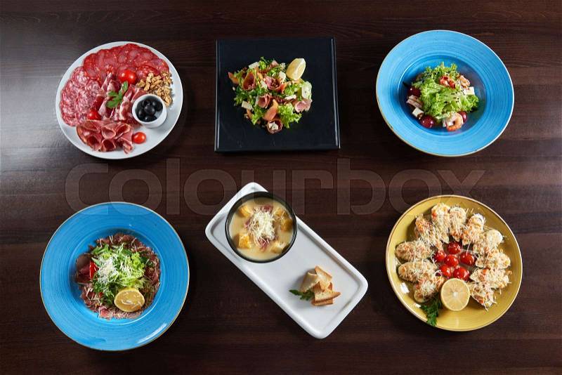 Food heaven. Top view of a restaurant table with plates of salads bowl of soup assorted cold meet appetizers and shellfish mussels baked with cheese, stock photo