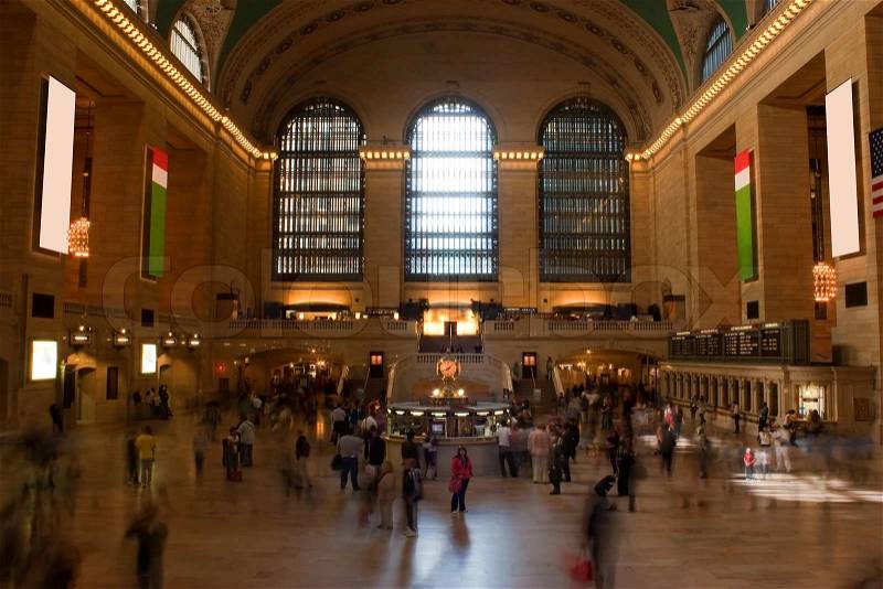 Time lapse photo of blurred people walking through Grand Central Terminal train station in New York City with one recognizable woman standing alone in the center, stock photo