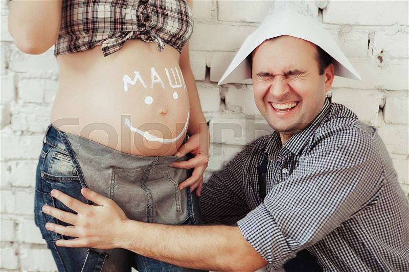 Young man paints happy smiley face on the belly of his pregnant wife. Concept about love and happiness, stock photo