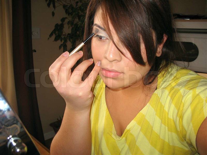 A young Spanish woman applying makeup in front of an illuminated cosmetic mirror, stock photo