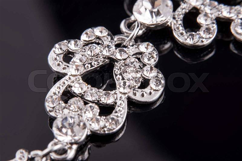 Cropped long silver or white gold earrings with diamonds and crystals on black reflective background. Macro photography. Fashion or shopping concept, stock photo