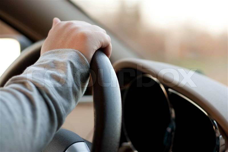 A woman holding the steering wheel of a car with one hand while driving, stock photo