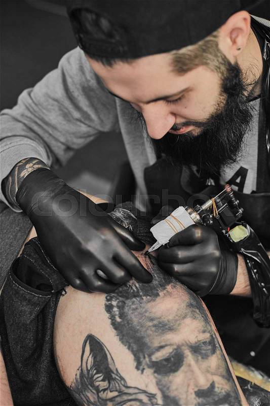 Tattoo master in black gloves, tattoo on the skin of black ink tattoo of his client in the salon, stock photo
