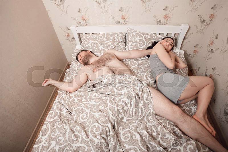 Couple sleeping problems concept. Man has occupied all bed, woman lies on the edge, stock photo