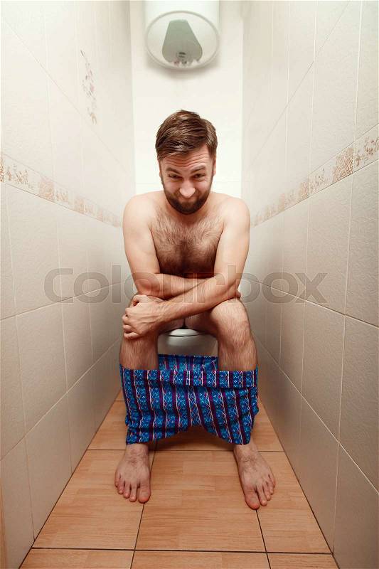 Man with lowered pants makes an effort on a toilet bowl, stock photo