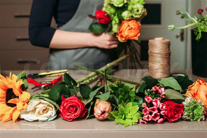 Florist with bouquet of roses at work. Woman in apron creating bouquet of flowers, stock photo