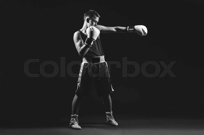 Young handsome boxer sportsman in white boxing gloves on black backgound. Copy space. Monochrome photo, stock photo